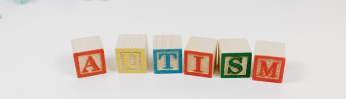 Wooden blocks spelling autism surrounded by colorful toys on a white background.